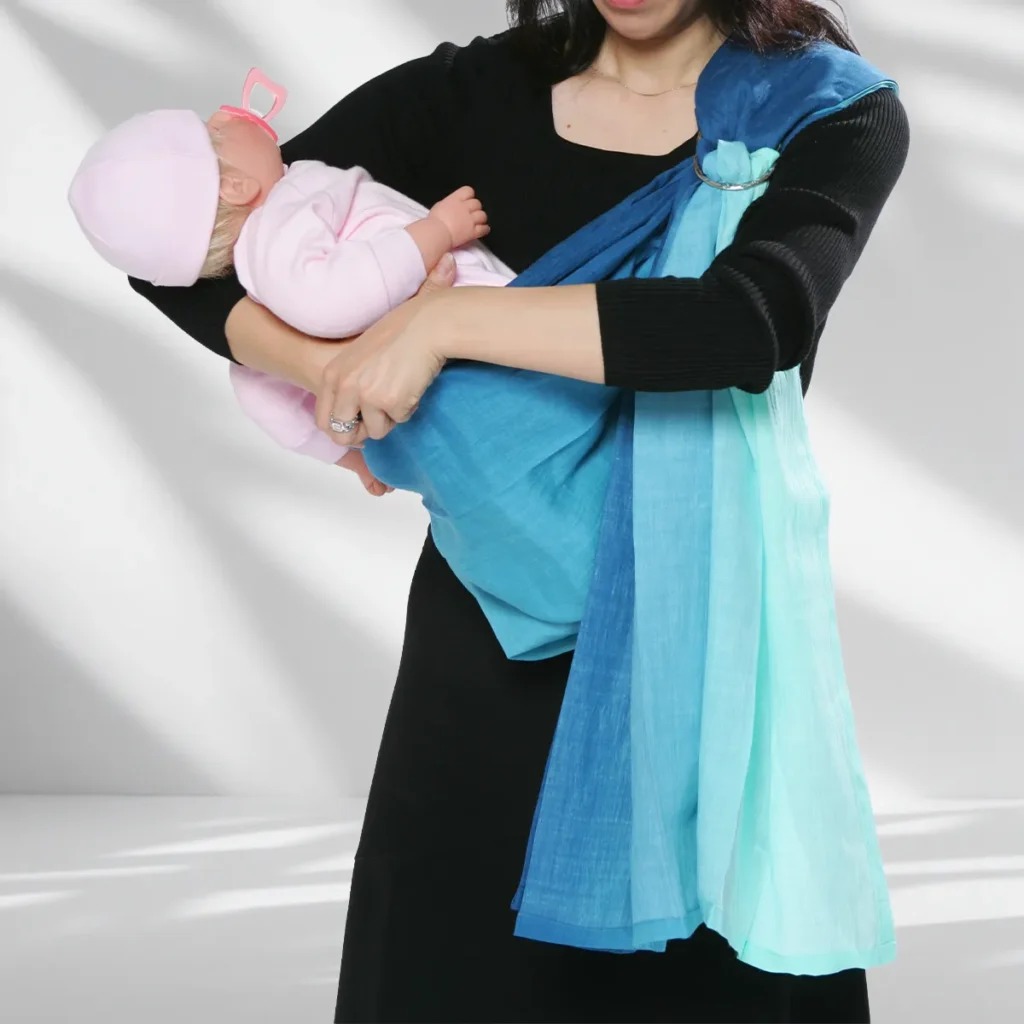赤ちゃんを迎え入れる:スリングを左肩にかけたモデルが、赤ちゃんを抱き上げながら、左手でスリングのポーチを開いて赤ちゃんの足を迎え入れようとしている状態